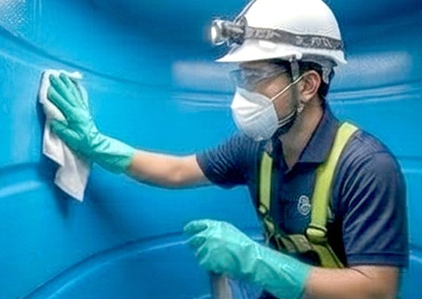 CPM Water Solution technician hand-cleaning the inner walls of a tank
